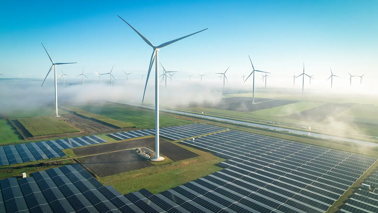 Aerial view of a solar energy field and wind turbines in foggy conditions during a Autumn morning.