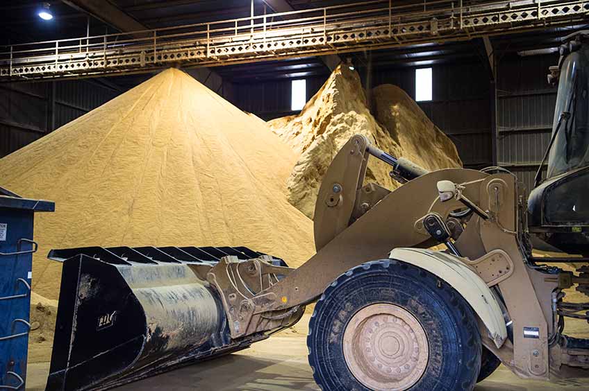 Photo of a warehouse containing a large pile of grains with a yellow tractor in the foreground.