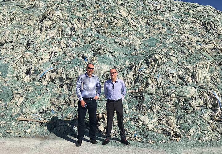 Photo of two men standing in front of a giant pile of trash.