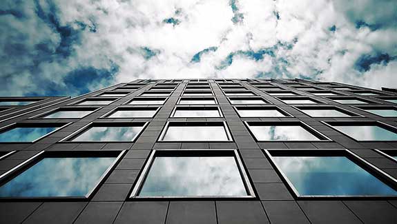 Photo of a building and sky with clouds, reflections of the clouds appear in the windows of the building.